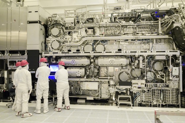 The ASML High-NA EUV lithography machine in a cleanroom: a wall of stainless-steel modules with a large module suspended above it.